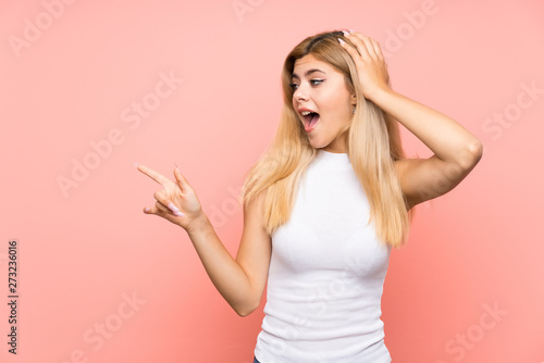 Teenager girl over isolated pink background surprised and pointing finger to the side