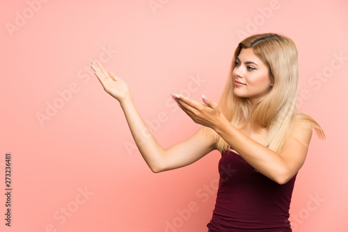 Teenager girl over isolated pink background extending hands to the side for inviting to come