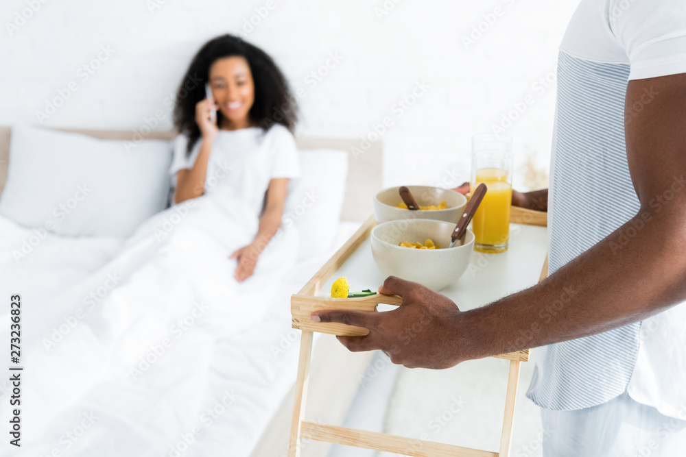 selective focus of african american man holding try with breakfast, on smiling girlfriend background selective focus of african american man holding try with breakfast, on smiling girlfriend background