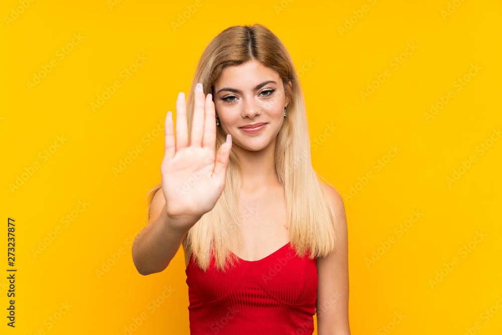 Teenager girl over isolated yellow background making stop gesture with her hand Teenager girl over isolated yellow background making stop gesture with her hand