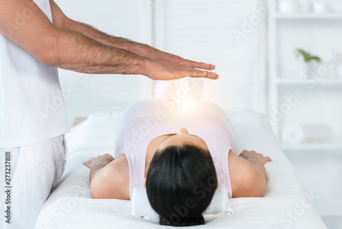 Fotografie cropped view of healer putting hands above body of brunette woman lying on massa