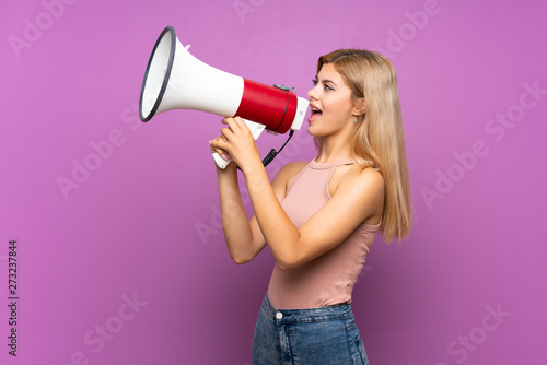 Teenager girl over isolated purple background shouting through a megaphone