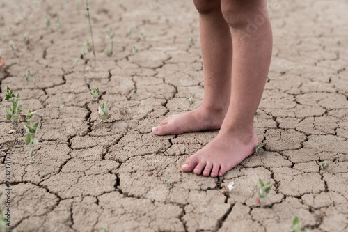 Bare feet of a child on dried cracked earth. The concept of lack of water, thirst. © Konstiantyn Zapylaie