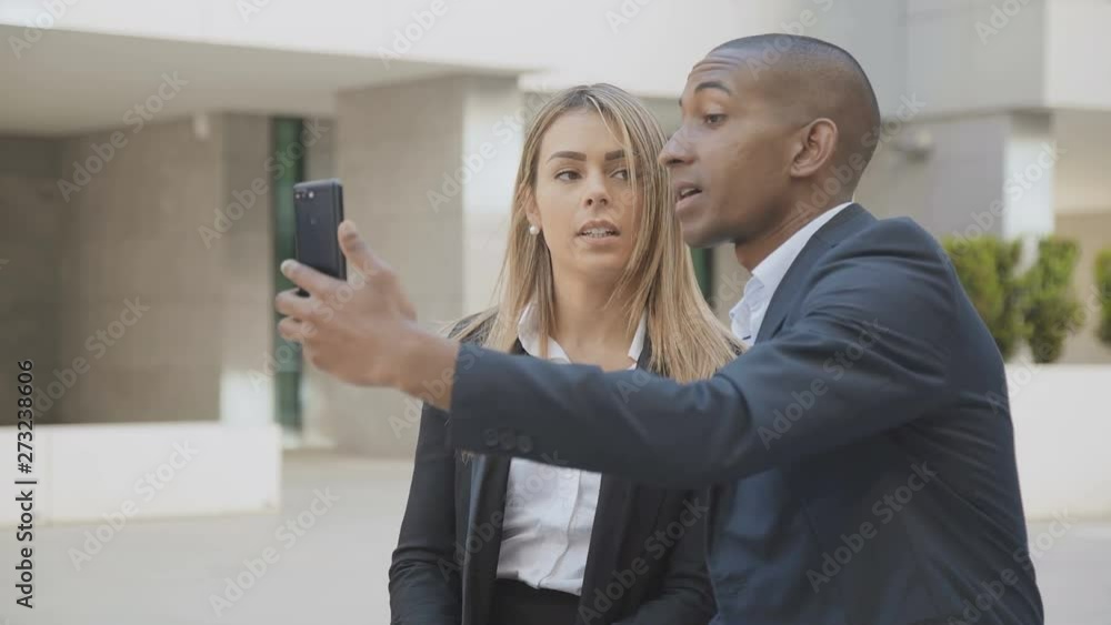 Serious business colleagues answering video call. Multiethnic young businessman and businesswoman talking during video conversation via smartphone outdoor. Technology concept Serious business colleagues answering video call. Multiethnic young businessman and businesswoman talking during video conversation via smartphone outdoor. Technology concept