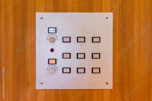 White control panel on a wooden wall with white, blue and red buttons and regulators