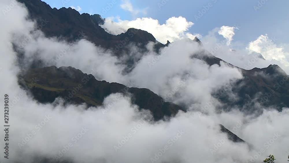 A still long shot of the terrain as the heavy mist settles on the peak of the mountains with the sun shining through the blue and cloudy sky on a warm afternoon A still long shot of the terrain as the heavy mist settles on the peak of the mountains with the sun shining through the blue and cloudy sky on a warm afternoon