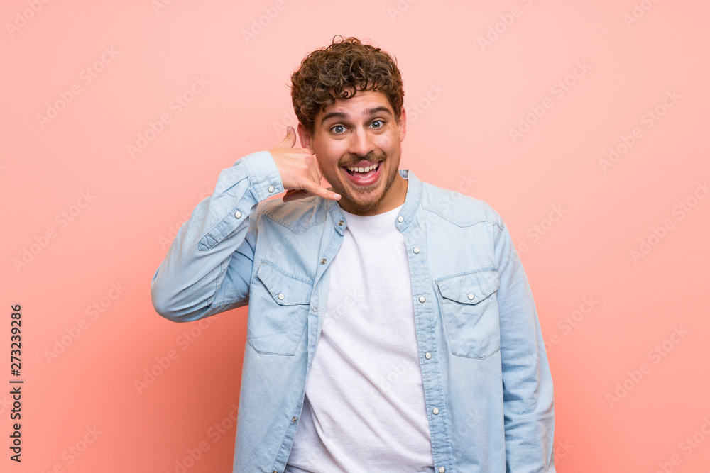 Blonde man over pink wall making phone gesture. Call me back sign Blonde man over pink wall making phone gesture. Call me back sign