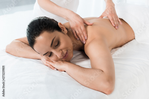 cropped view of masseur doing massage to happy brunette woman lying on massage table