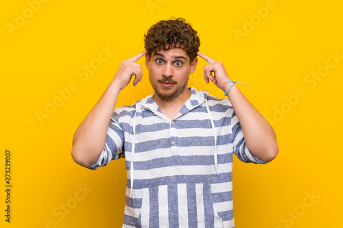 Blonde man over yellow wall having doubts and thinking