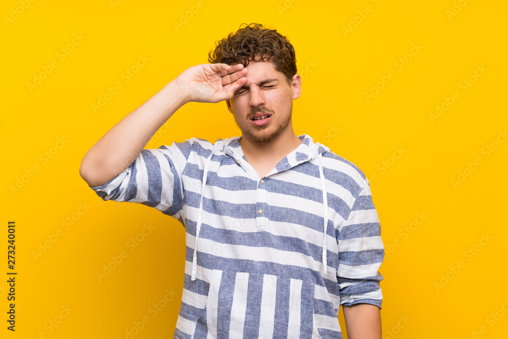 Blonde man over yellow wall with tired and sick expression Blonde man over yellow wall with tired and sick expression