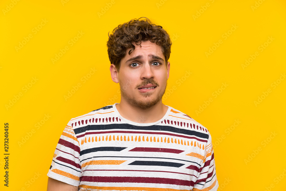 Blonde man over yellow wall having doubts and with confuse face expression Blonde man over yellow wall having doubts and with confuse face expression