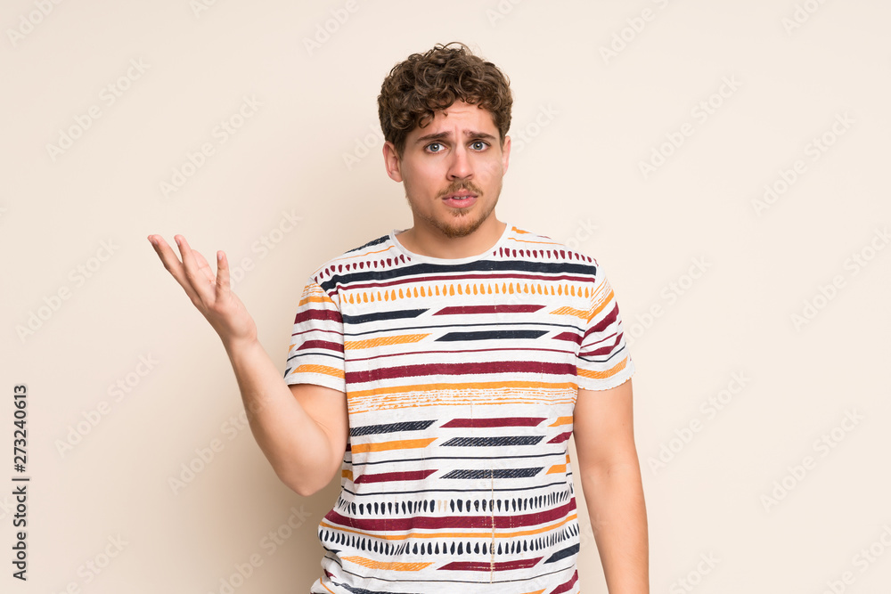Blonde man over isolated wall making doubts gesture Blonde man over isolated wall making doubts gesture