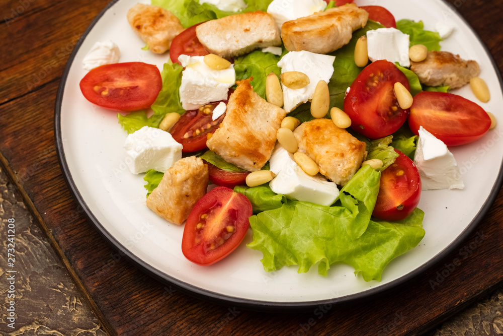 Salad with warm chicken, cherry tomatoes and soft brynza cheese, decorated with pine nuts. dressing with olive oil. Plate with dish on old cutting board Salad with warm chicken, cherry tomatoes and soft brynza cheese, decorated with pine nuts. dressing with olive oil. Plate with dish on old cutting board