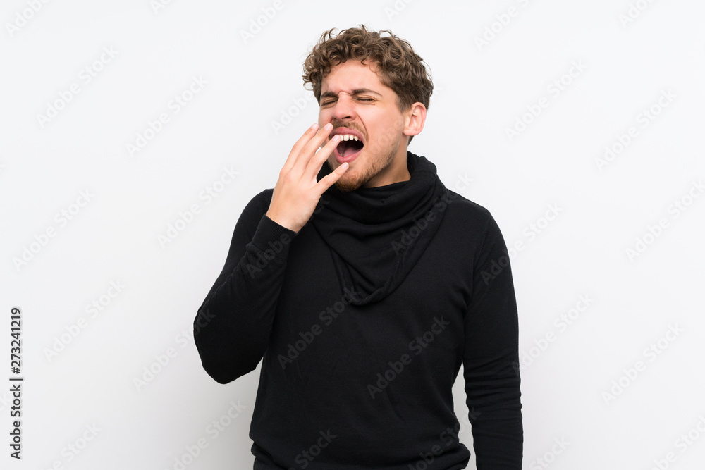 Blonde man over isolated white wall yawning and covering wide open mouth with hand