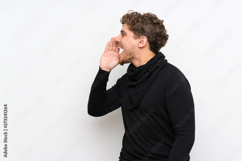 Blonde man over isolated white wall shouting with mouth wide open to the lateral Blonde man over isolated white wall shouting with mouth wide open to the lateral