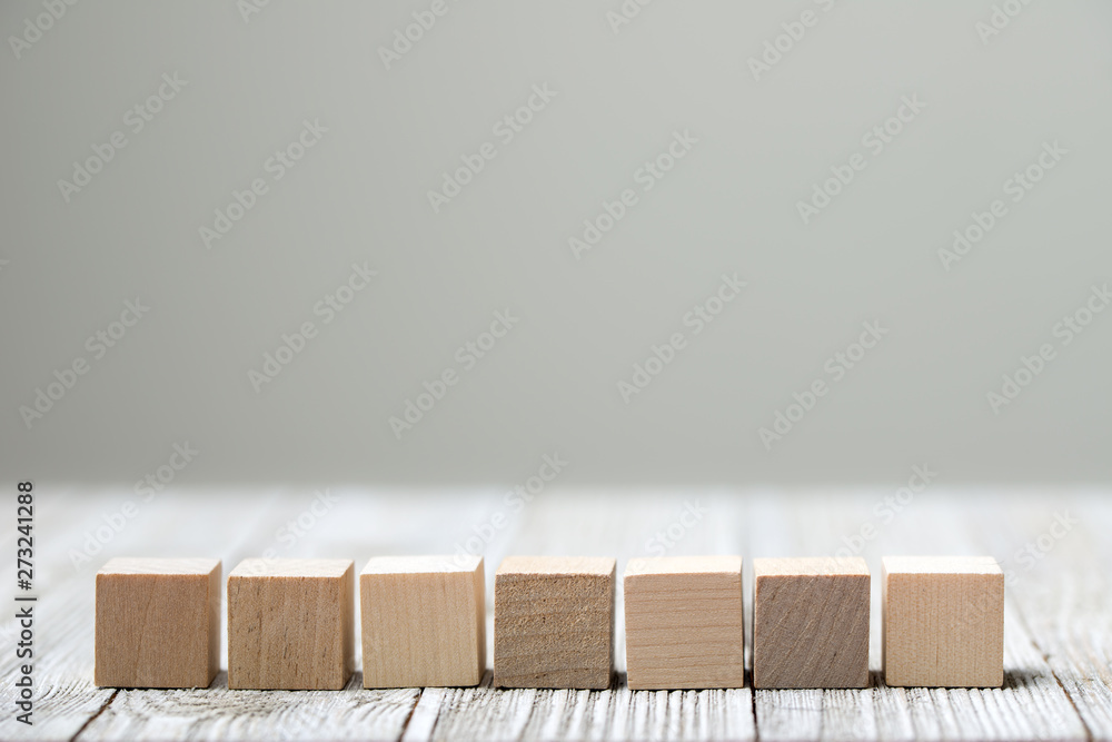 Seven wooden toy cubes arranged in row on white grey wooden background Seven wooden toy cubes arranged in row on white grey wooden background