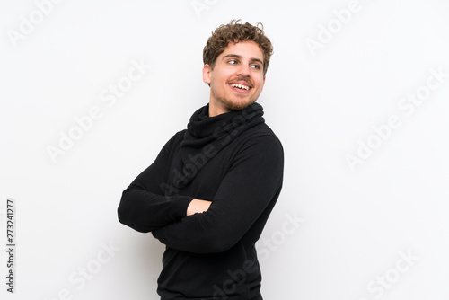 Blonde man over isolated white wall with arms crossed and happy
