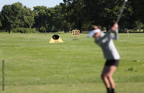 a young girl practice golf by aiming at targets on a driving range