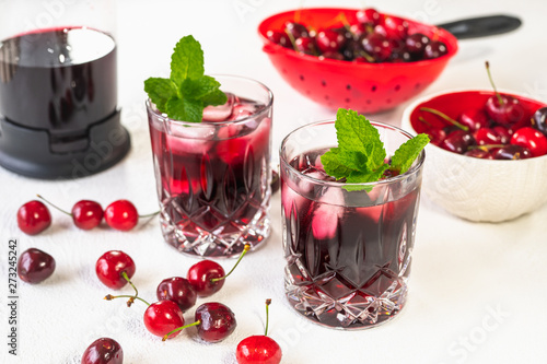 Fresh Cold Cherry Juice in Glasses with Mint Leaves and Ice, and Cherries in a Bowl on White background Close Up