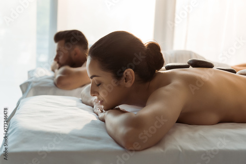 selective focus of brunette woman with closed eyes having stone massage near man