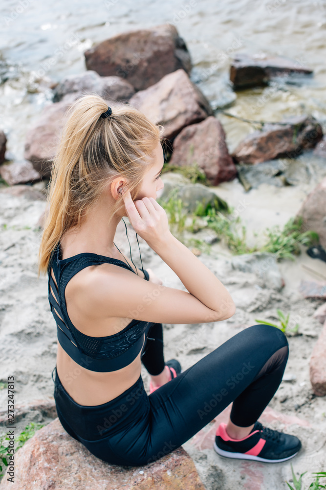 overhead view of athletic woman sitting on stone while listening music in earphones