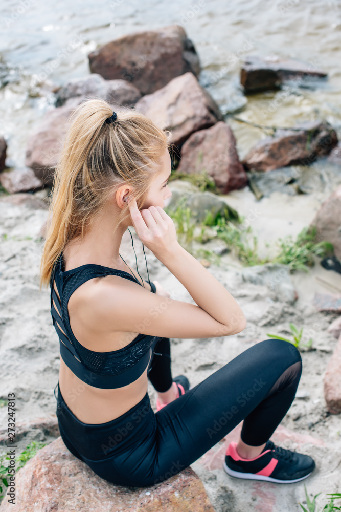 overhead view of athletic woman sitting on stone while listening music in earphones overhead view of athletic woman sitting on stone while listening music in earphones