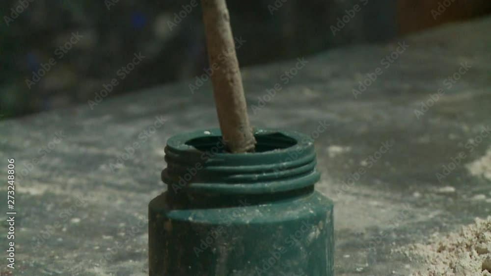 A tilting close up shot of a black long brush in a green container which is placed on a steel table with some powder stains on it. A tilting close up shot of a black long brush in a green container which is placed on a steel table with some powder stains on it.