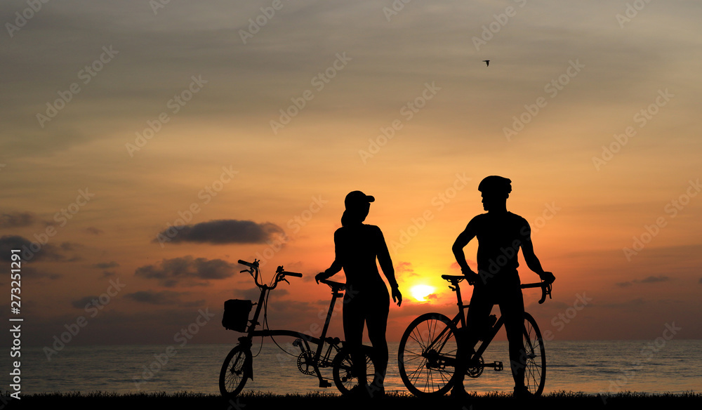 Obraz premium Silhouette couple and bike relaxing on blurry sunset background.