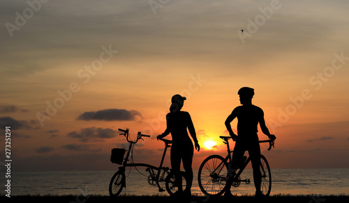 Silhouette couple and bike relaxing on blurry sunset background.