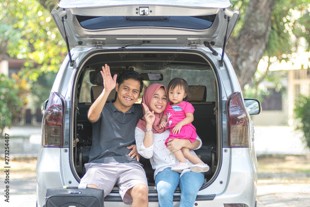 young muslim family , transport, leisure, road trip and people concept - happy man, woman and little girl sitting on trunk of hatchback car and waving hand outdoors young muslim family , transport, leisure, road trip and people concept - happy man, woman and little girl sitting on trunk of hatchback car and waving hand outdoors