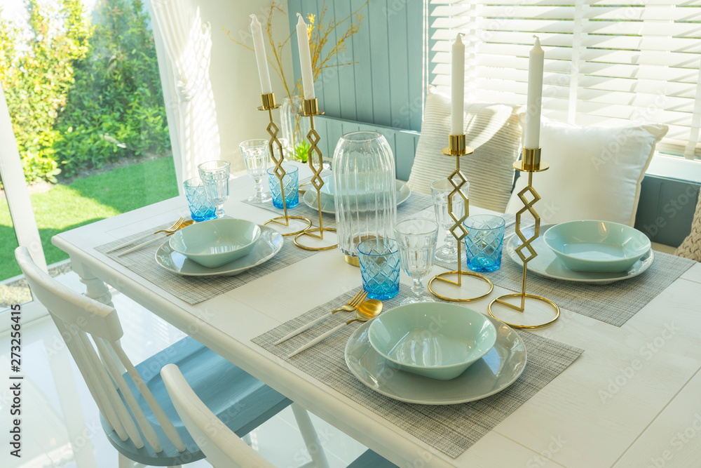 Pale blue plate setting on table with gold candle holder in home dining room interior. 