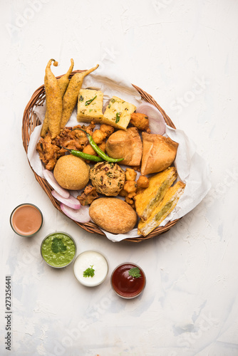 Indian Tea time snacks  in group includes Veg Samosa, Kachori/kachaudi, aloo bonda, khaman dhokla, bread, onion,chilli and moong pakora/pakoda/bhaji/bhajji/Bhajiya/bajji with sauces, selective focus photo