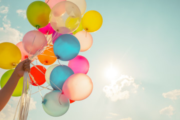 Hand holding multi colored balloons done with a retro vintage instagram filter effect.