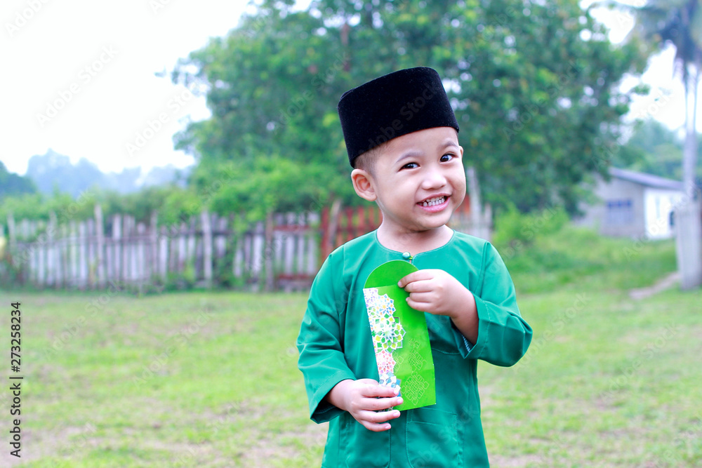 A Malay boy in Malay traditional cloth showing his happy reaction after received money pocket during Eid Fitri or Hari Raya celebration. A Malay boy in Malay traditional cloth showing his happy reaction after received money pocket during Eid Fitri or Hari Raya celebration.