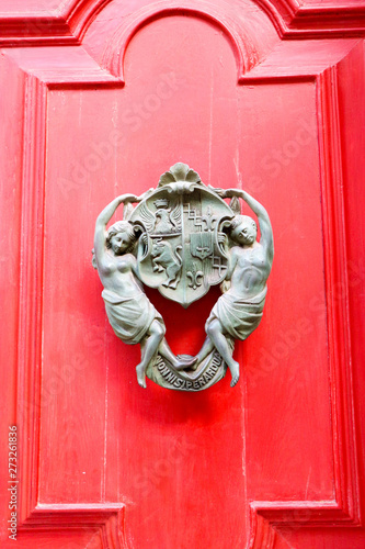 Vintage bronze two woman with coat of arms in their hands door handle on red wooden door, Luqa, Malta photo