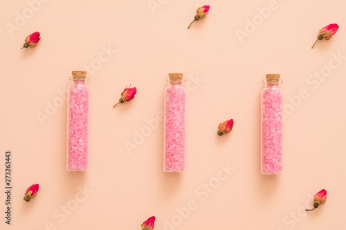Rose essential oil diy bath salt in glass bottles. Floral pattern peach background.
