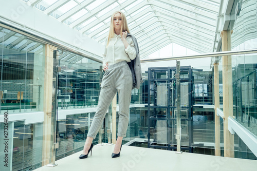 Young elegant business woman in a stylish gray suit pants and jacket in a modern office with panoramic windows shopping center