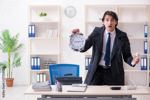 Young male employee in the office in time management concept 