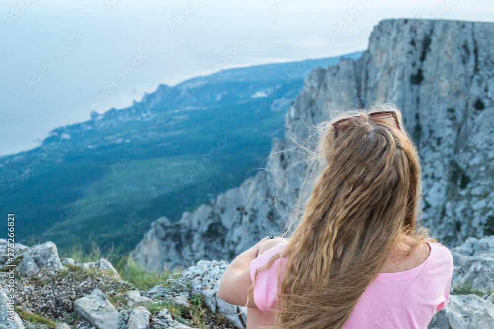 Naklejka premium girl with long blond hair sits on top of Mount Ai-Petri in Crimea with a sea view
