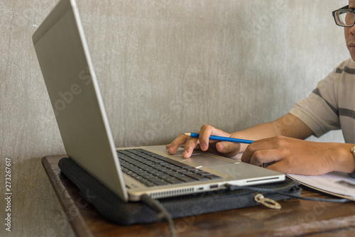 Asian student holding pen while using laptop 