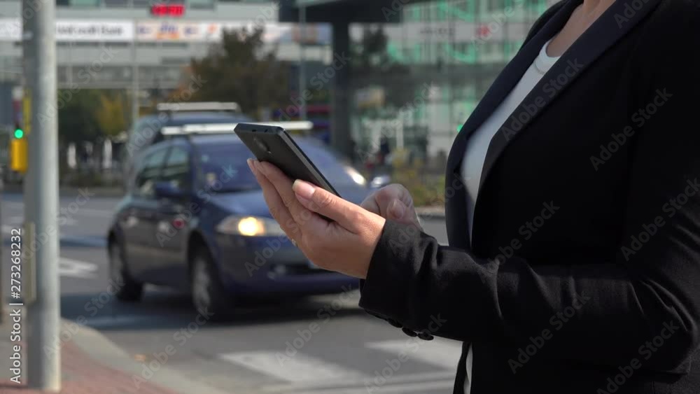 A businesswoman works on a smartphone in a street in an urban area on a sunny day - closeup - a busy road in the blurry background A businesswoman works on a smartphone in a street in an urban area on a sunny day - closeup - a busy road in the blurry background