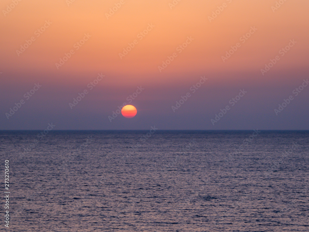 A stunning sunset over the sea. Sun sets directly into the water. Sky is dark orange and the water has a darker shade. Night wins over the day. Paphos, Cyprus.