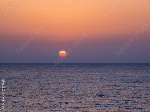 A stunning sunset over the sea. Sun sets directly into the water. Sky is dark orange and the water has a darker shade. Night wins over the day. Paphos  Cyprus.