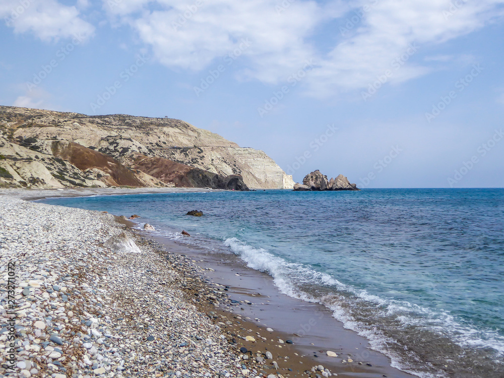 A rocky Aphrodite's beach in Petra tou Romiou, Cyprus. Beach stretches far away, surrounded by steep cliffs. Water has a turquoise shade. Idyllic and calm place. Waves slowly wash the shore
