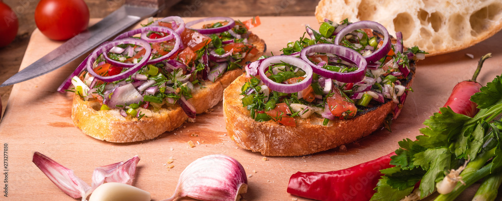 Italian delicious vegan bruschetta with raw chopped tomatoes, chili peppers, spring greens and red onions, herbs and olive oil on a cutting board close-up - rustic style