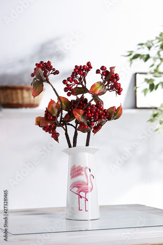 Shot of an interior design. The floral composition is in middle, with bunch of briar twigs in ceramic vase with literal and bird print. On blurred background there is wall shelf with photo frame. photo