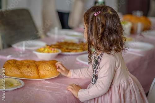 Little jewish curly girl placing challah bread on a table for Shabbat meal. photo