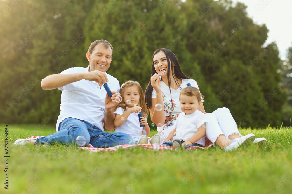 Happy family has fun playing with soap bubbles on the grass in the park. Happy family has fun playing with soap bubbles on the grass in the park.