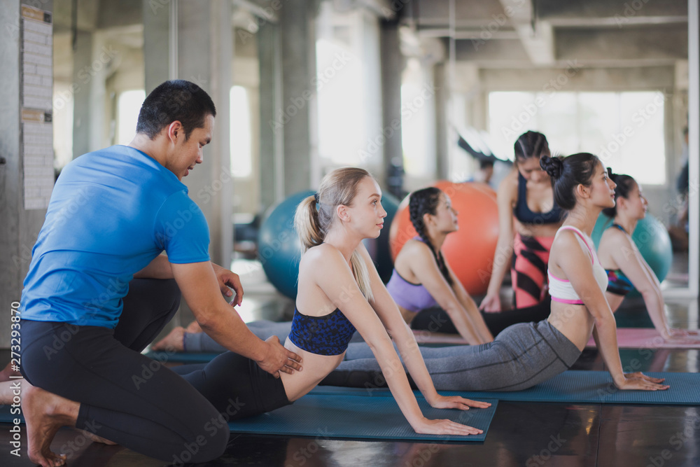 Group of young woman are stretching the body before exercise under coaching or trainer advise them at the gym. Woman workout and training yoga at fitness room concept. Group of young woman are stretching the body before exercise under coaching or trainer advise them at the gym. Woman workout and training yoga at fitness room concept.