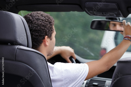 young male driver adjusting rear view mirror in car